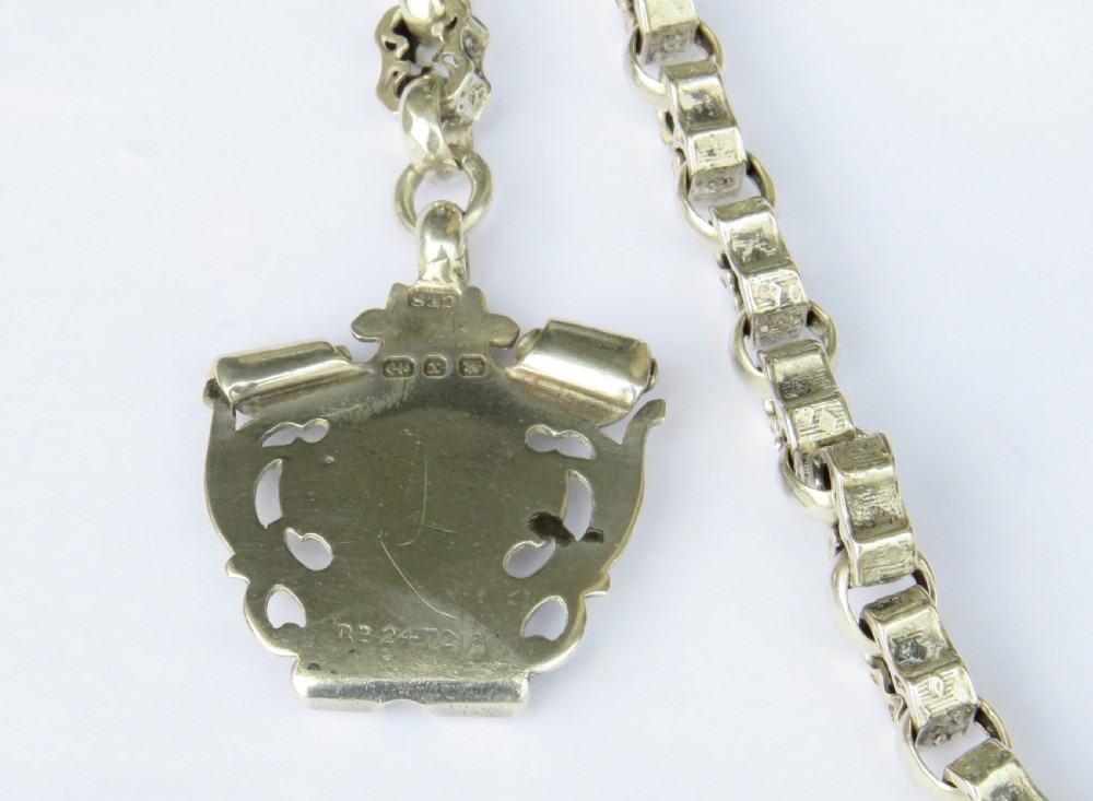 An antique sterling silver Albert watch chain featuring patterned fancy links, a T-bar fastener, a swivel clip, and a shield-shaped fob with a gold cartouche. View III