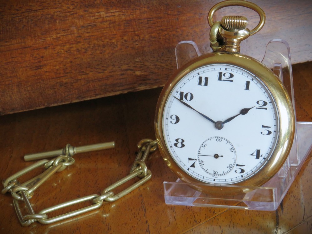 An open-face gold-tone pocket watch featuring a white enamel dial with black Arabic numerals, sub-seconds dial, and attached T-bar chain.