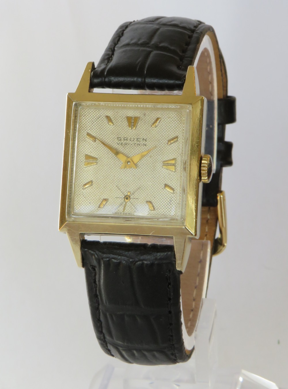 A gents vintage 1950s square gold-cased Gruen Veri-Thin wristwatch with a textured dial and a black alligator-grain leather strap.
