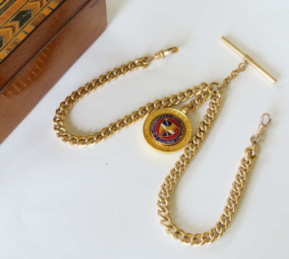 A gold filled double Albert watch chain featuring heavy curb links, a central T-bar, two swivel clasps, and a circular enamelled fob.