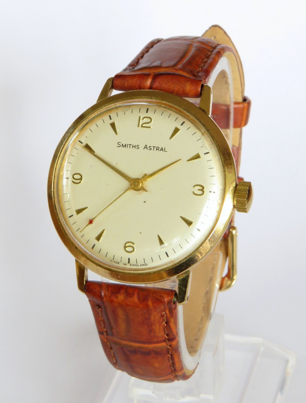 A 1960s Smiths Astral wristwatch featuring a gold-plated case, a cream dial with Arabic numerals at twelve, three, six, and nine, and a brown leather strap.