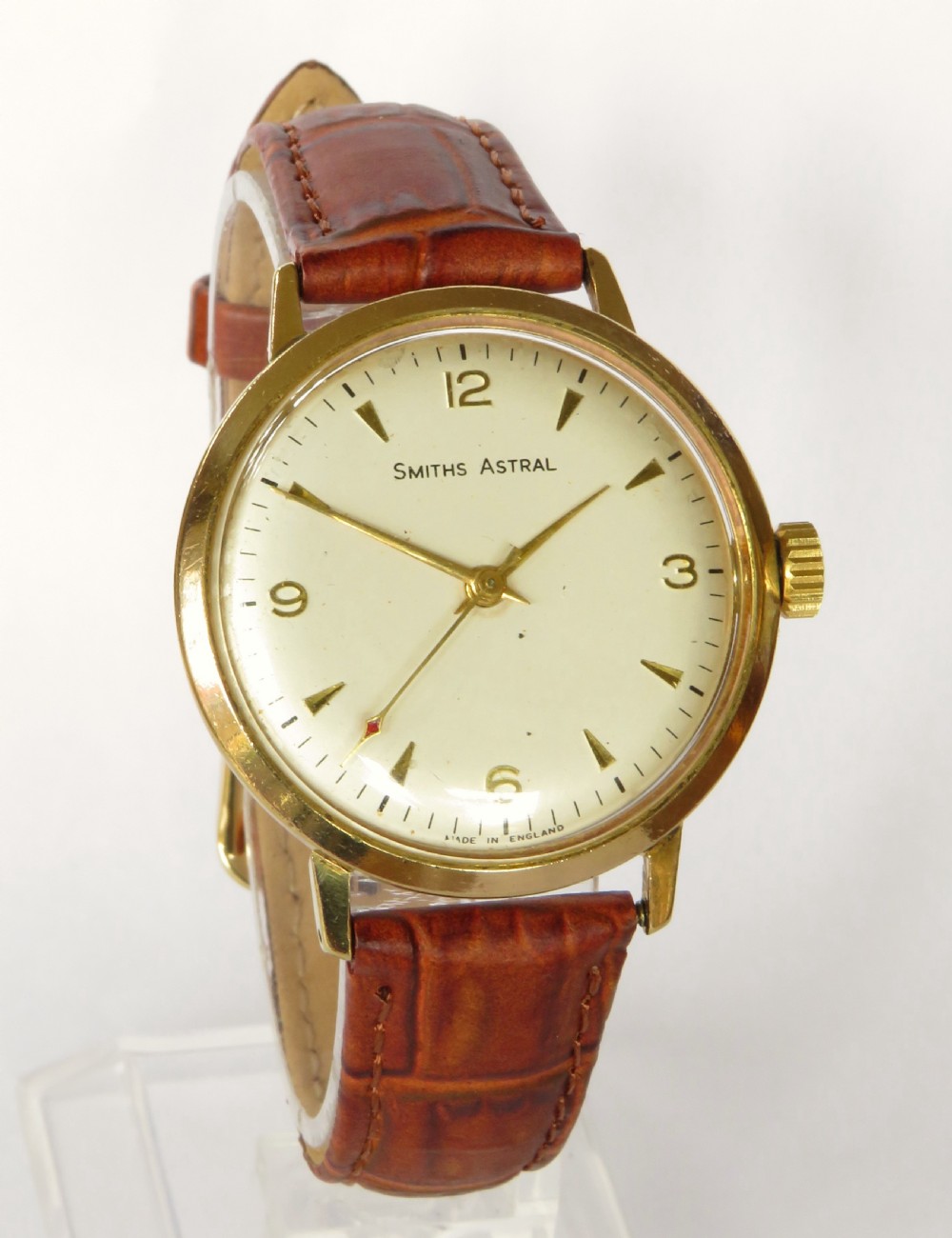 A 1960s Smiths Astral wristwatch featuring a gold-plated case, a cream dial with Arabic numerals at twelve, three, six, and nine, and a brown leather strap. View II