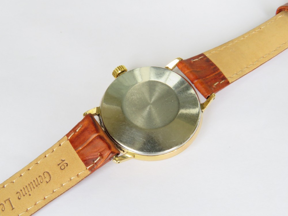 A 1960s Smiths Astral wristwatch featuring a gold-plated case, a cream dial with Arabic numerals at twelve, three, six, and nine, and a brown leather strap. View IV