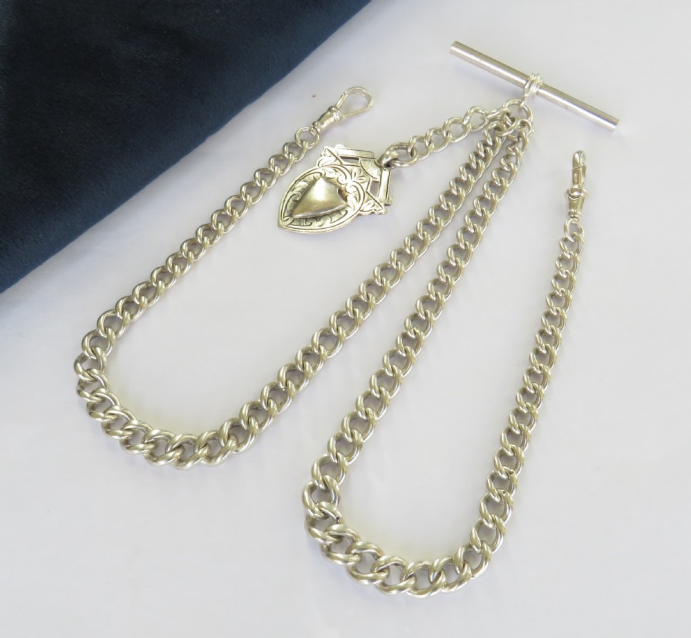 A silver double curb link Albert watch chain necklace featuring a central T-bar, swivel clasps, and an engraved shield fob.