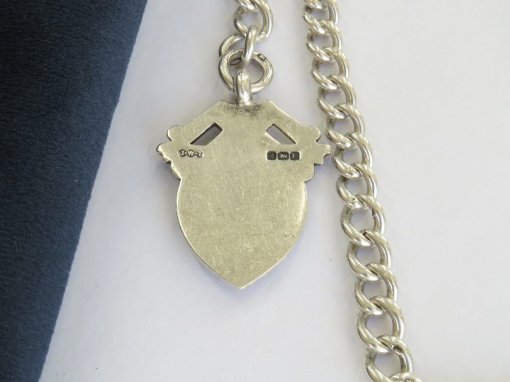 A silver double curb link Albert watch chain necklace featuring a central T-bar, swivel clasps, and an engraved shield fob. View IV
