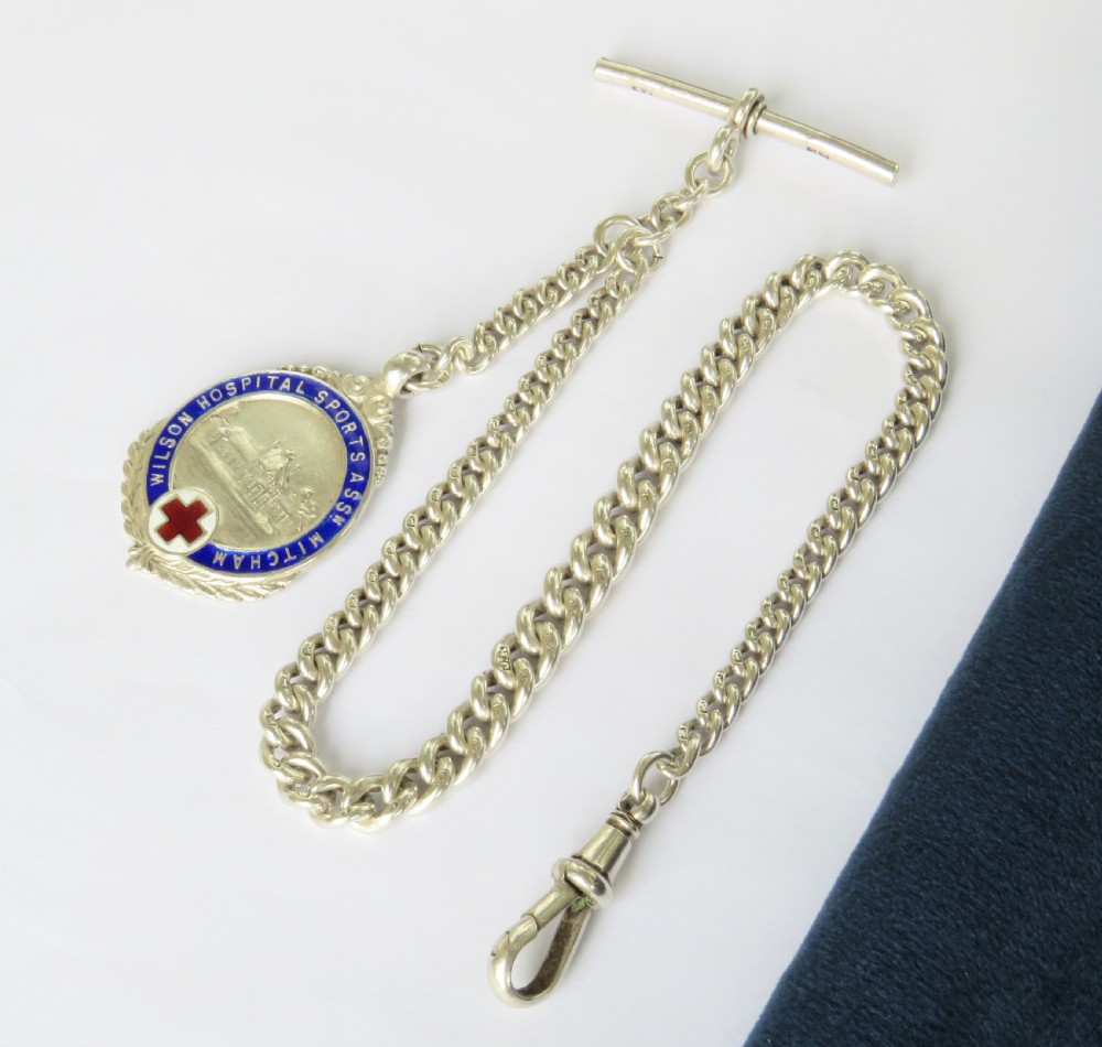 A sterling silver curb-link pocket watch chain featuring a T-bar fastener, swivel clasp, and a circular blue and red enamel sports medallion.