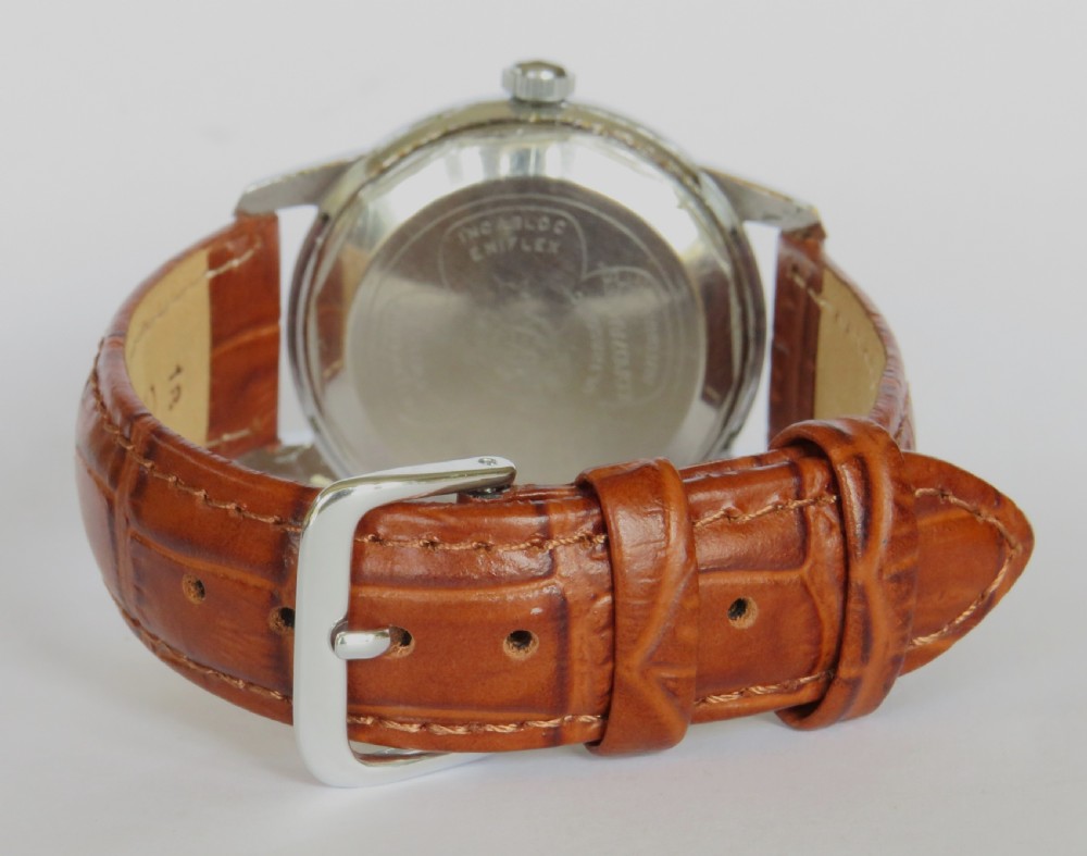 A 1950s mens Enicar Ultrasonic automatic wristwatch featuring a circular silver-tone case, cream dial with hour batons, date window, and a brown leather strap. View IV