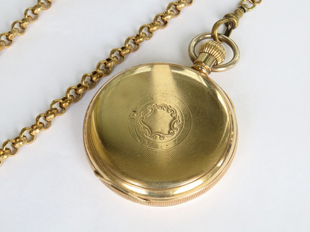 A 1930s gold-toned open-face pocket watch featuring a white enamel dial with Arabic numerals, a sub-seconds register, and a connected Albert chain with T-bar. View V