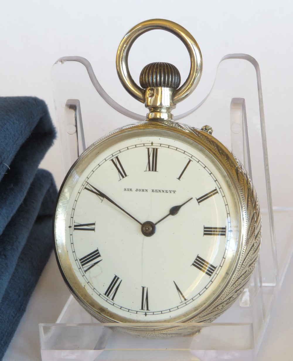 An antique open-face silver pocket watch featuring a white enamel dial with black Roman numerals and an engraved silver case.