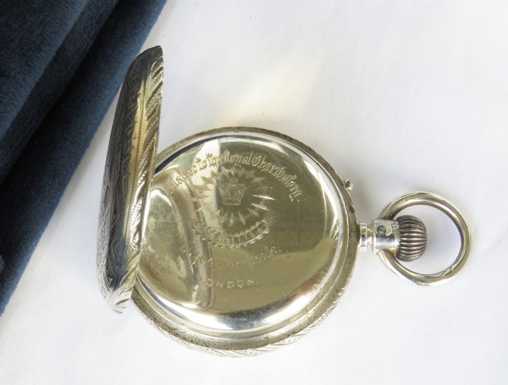 An antique open-face silver pocket watch featuring a white enamel dial with black Roman numerals and an engraved silver case. View III