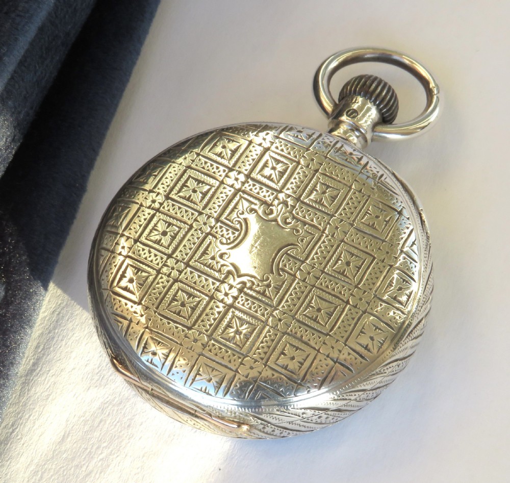 An antique open-face silver pocket watch featuring a white enamel dial with black Roman numerals and an engraved silver case. View V