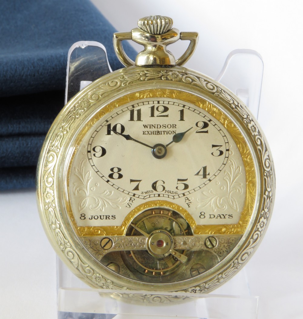 An open-faced 1930s Windsor Exhibition pocket watch featuring an engraved silver-tone case, gilt accents, and a visible balance wheel at the six oclock position. View II