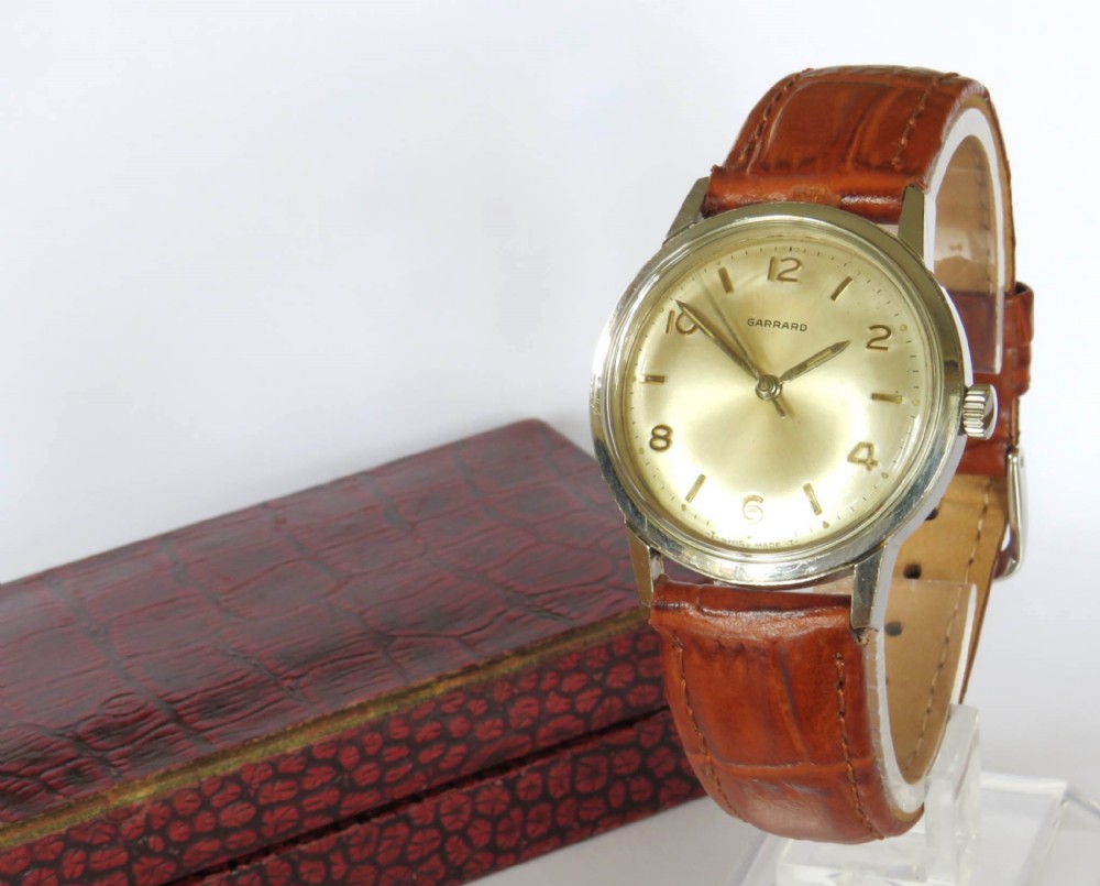 A 1960s Garrard gents wristwatch featuring a champagne gold dial with Arabic numerals and a cognac brown leather strap.