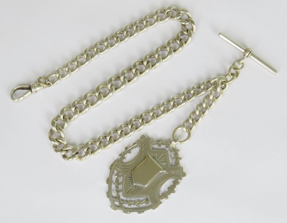 A Victorian sterling silver heavy curb link Albert watch chain featuring a T-bar attachment, swivel clasp, and an engraved shield-shaped fob.