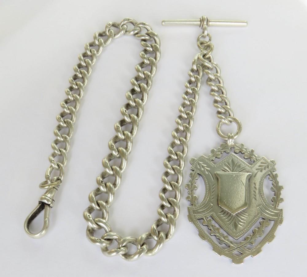 A Victorian sterling silver heavy curb link Albert watch chain featuring a T-bar attachment, swivel clasp, and an engraved shield-shaped fob. View II