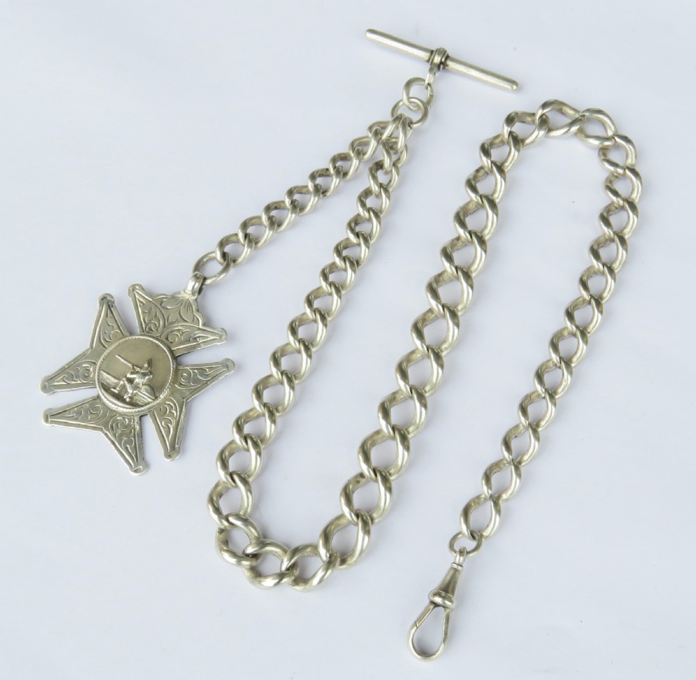 A silver curb link Albert pocket watch chain featuring a T-bar fastener, swivel clasp, and a carved star-shaped fob medallion.