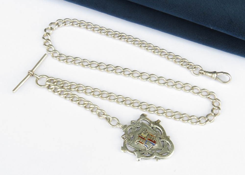 An antique silver curb link pocket watch chain featuring a T-bar, swivel clasp, and a heraldic enamelled shield fob.