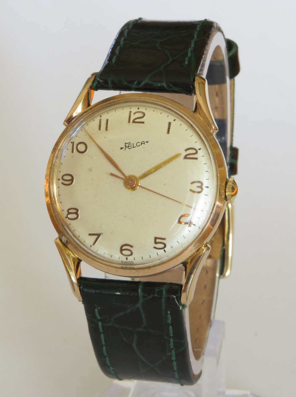 A 1960s gents Felca wristwatch featuring a gold-plated circular case, cream dial with Arabic numerals, and a dark green textured leather strap.