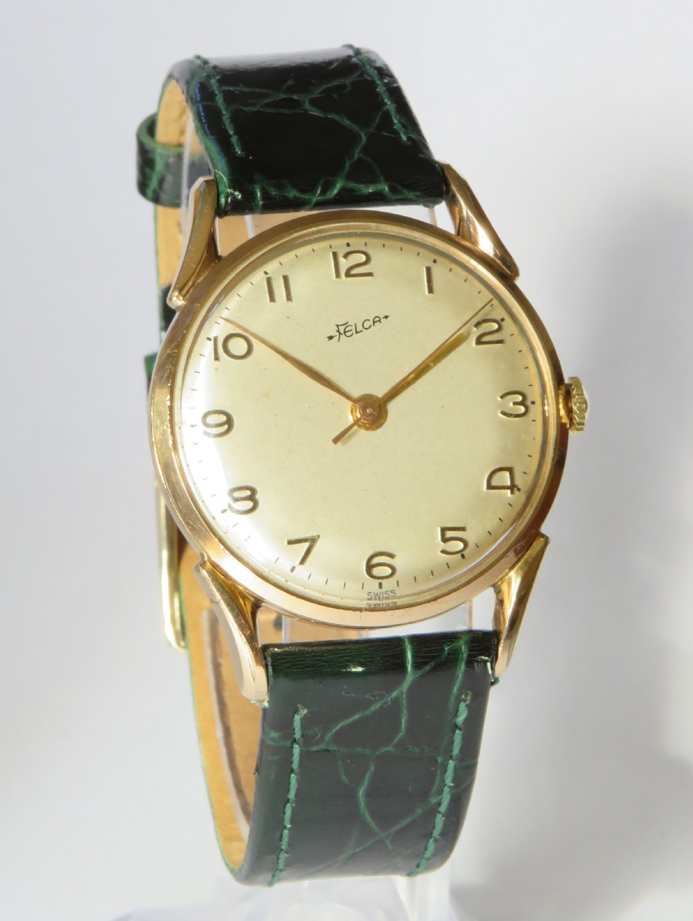 A 1960s gents Felca wristwatch featuring a gold-plated circular case, cream dial with Arabic numerals, and a dark green textured leather strap. View II