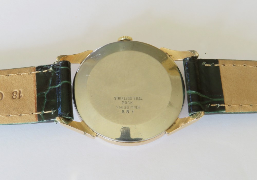 A 1960s gents Felca wristwatch featuring a gold-plated circular case, cream dial with Arabic numerals, and a dark green textured leather strap. View IV