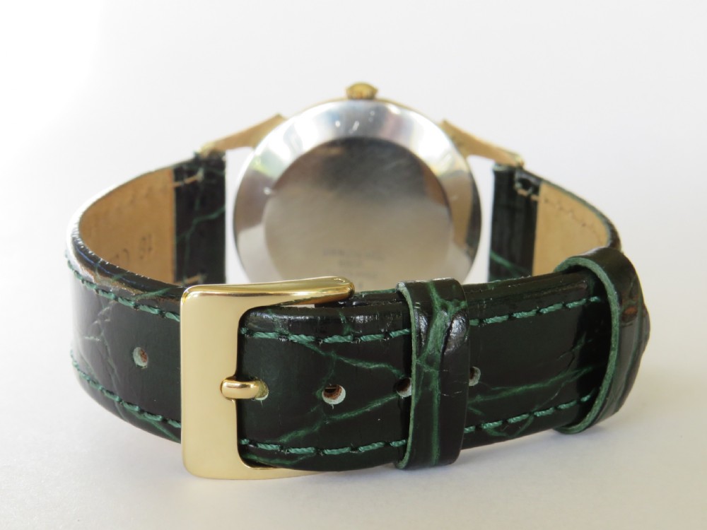 A 1960s gents Felca wristwatch featuring a gold-plated circular case, cream dial with Arabic numerals, and a dark green textured leather strap. View V