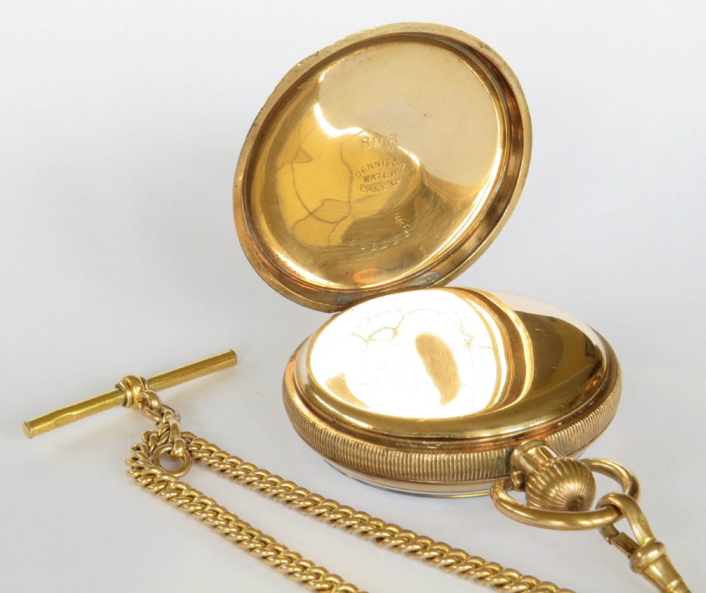 A 1920s gold-toned open-faced pocket watch displaying a white dial, black Arabic numerals, and a gold curb chain with a T-bar. View III