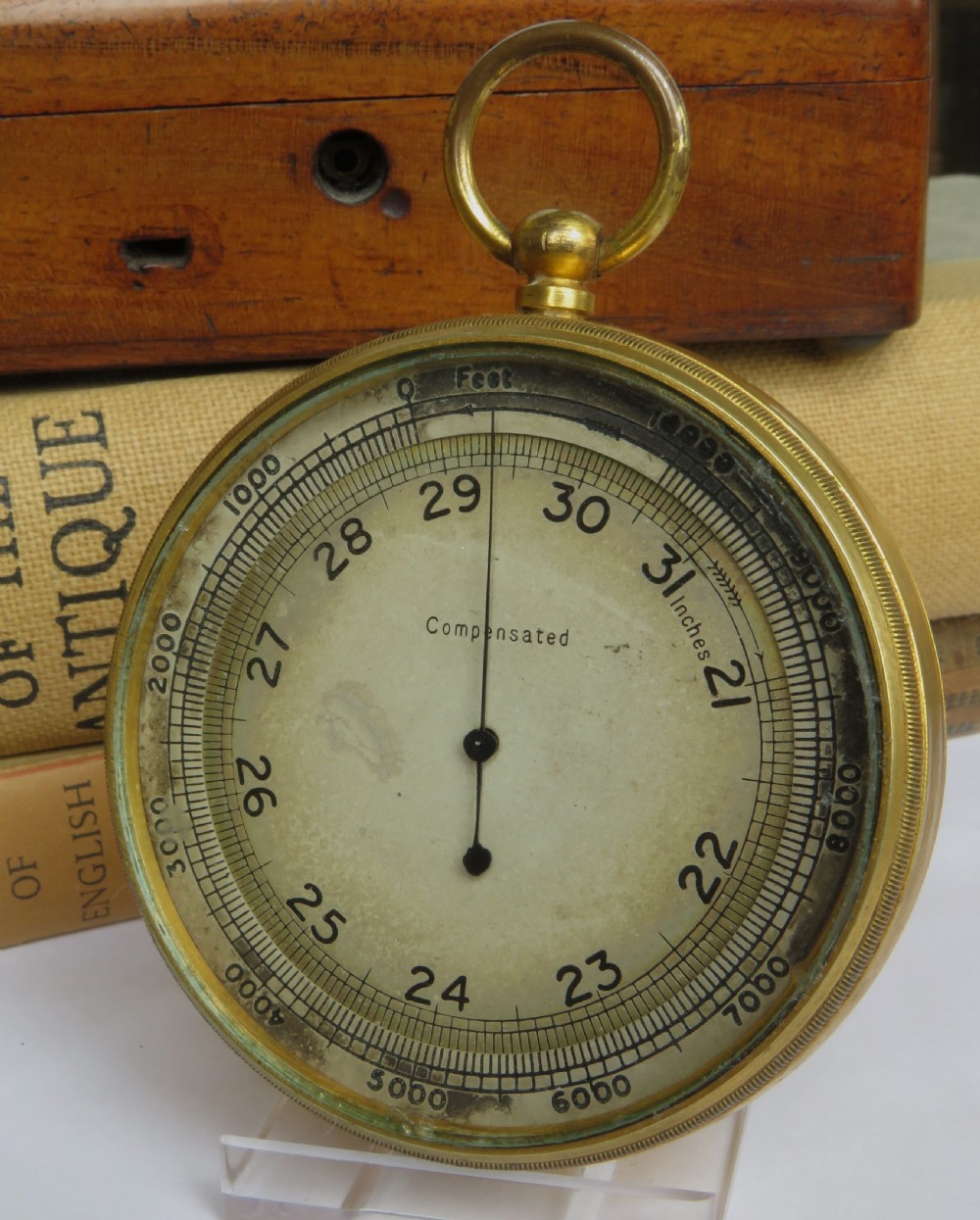 A circular antique brass pocket altimeter featuring a calibrated dial marked in feet and inches, with a top suspension loop.