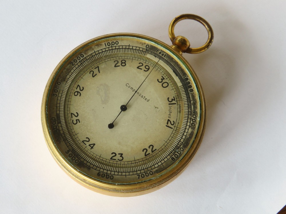 A circular antique brass pocket altimeter featuring a calibrated dial marked in feet and inches, with a top suspension loop. View II