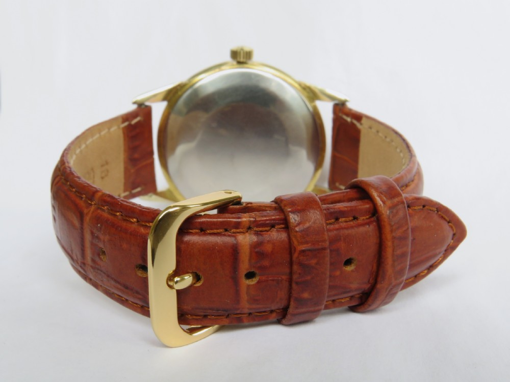 A 1960s Omega automatic wristwatch featuring a champagne dial with gold baton markers and a textured brown leather strap. View V