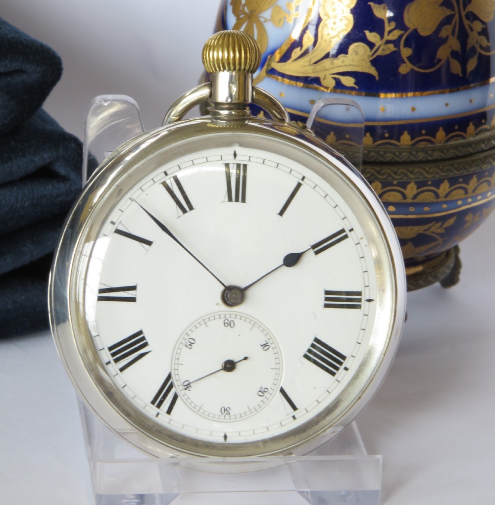 An open-faced silver pocket watch with a white enamel dial, black Roman numerals, a subsidiary seconds dial, and a ribbed brass onion crown. View II