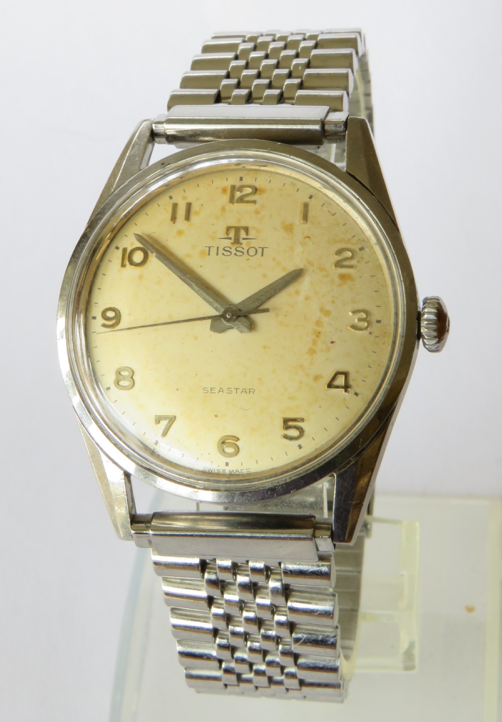 A vintage 1961 Tissot Seastar wrist watch featuring a stainless steel case, patinated cream dial with Arabic numerals, and a multi-link steel bracelet.