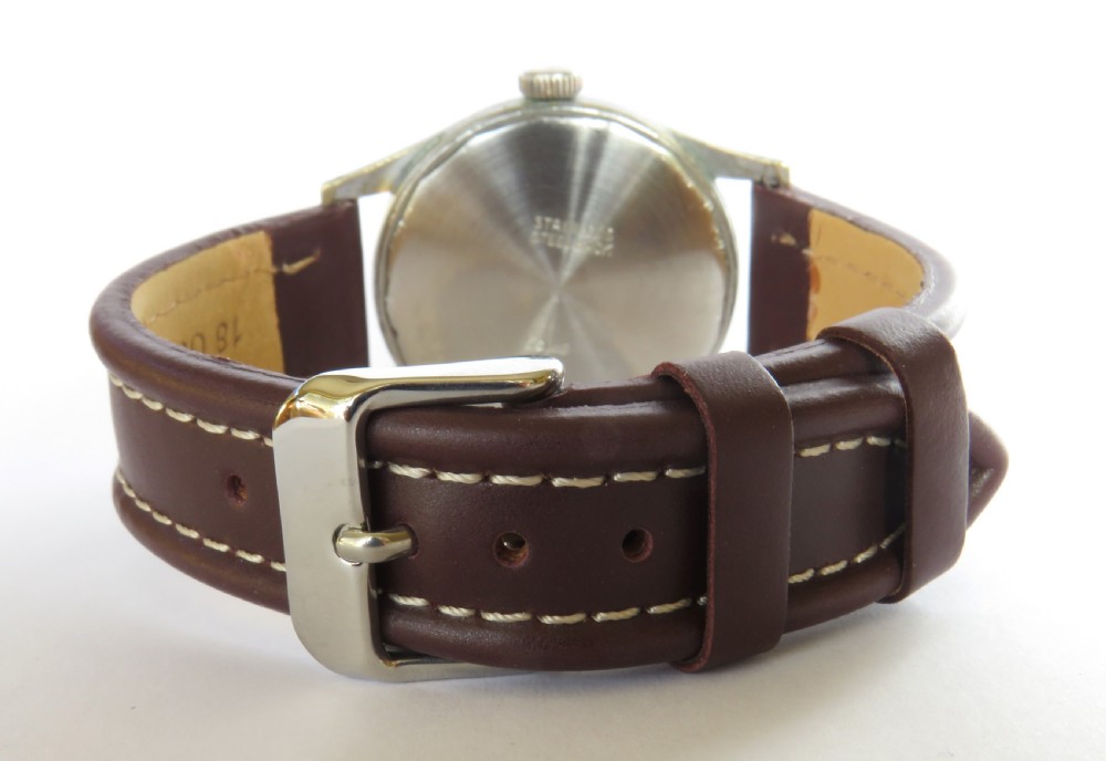A 1950s gents regulator wristwatch with a cream dial, twin sub-dials, a central red minute hand, a silver-tone metal case, and a stitched brown leather strap. View III
