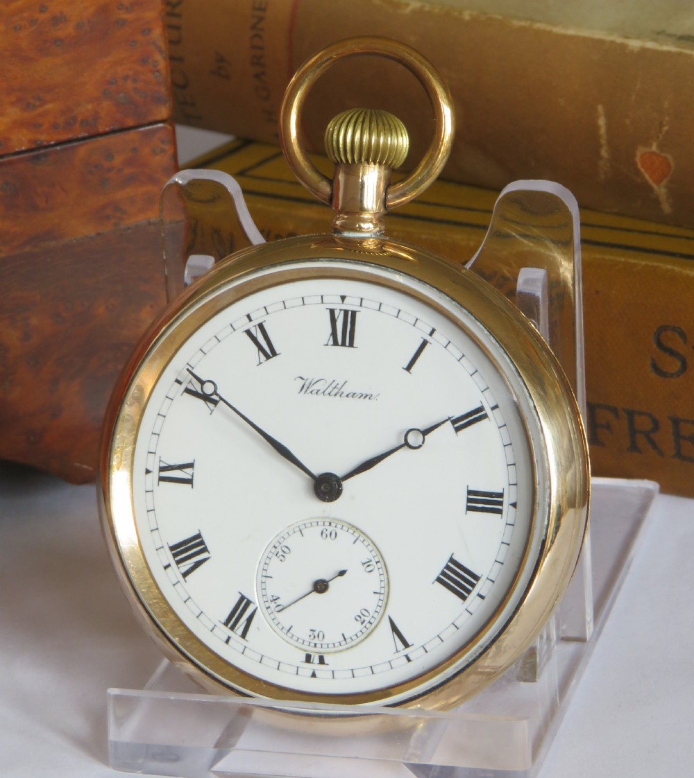 An open-face antique gold-tone pocket watch with a white enamel dial, black Roman numerals, and a secondary seconds dial at the bottom.