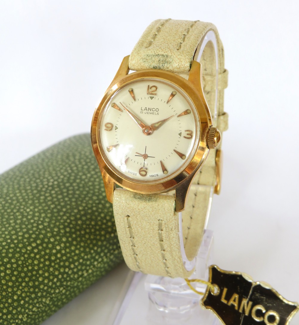 A 1950s gold-plated Lanco mechanical wrist watch with a cream dial and light leather strap resting inside its original green patterned presentation case. View II