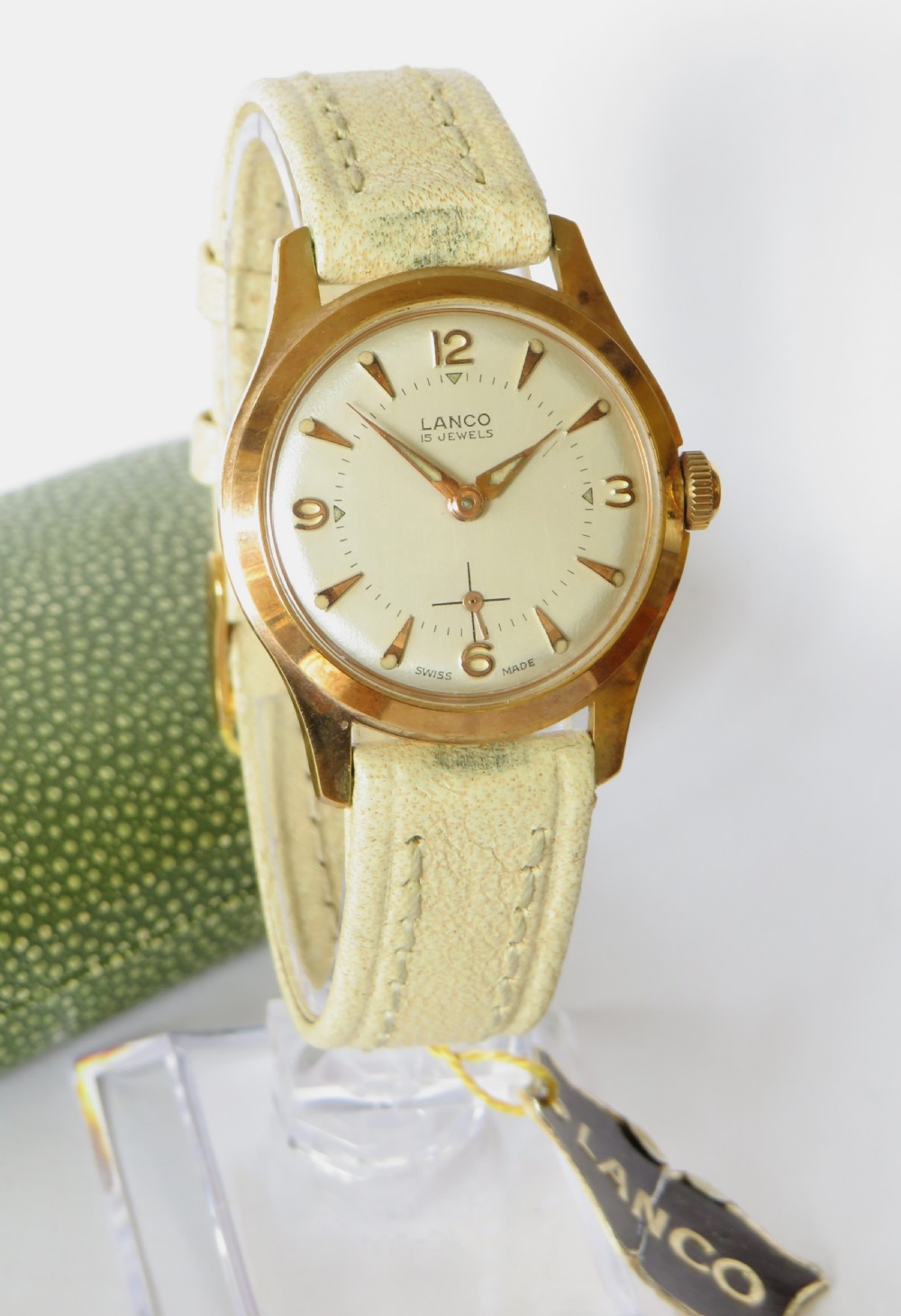A 1950s gold-plated Lanco mechanical wrist watch with a cream dial and light leather strap resting inside its original green patterned presentation case. View III