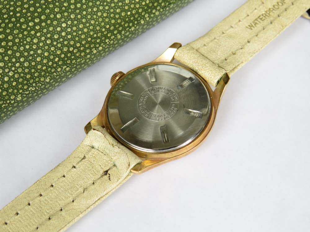 A 1950s gold-plated Lanco mechanical wrist watch with a cream dial and light leather strap resting inside its original green patterned presentation case. View IV