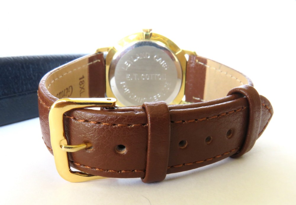 A 1960s gents Garrard wristwatch with a gold-toned case, off-white dial, baton markers, and brown leather strap resting inside a navy blue velvet presentation box. View V
