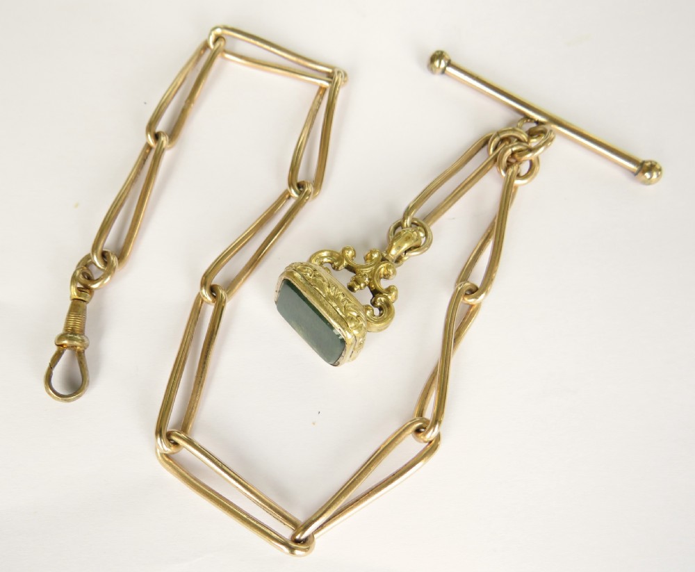 An antique Victorian rolled rose gold watch chain with elongated links, a T-bar attachment, a swivel clasp, and an ornamental fob seal with a green stone.