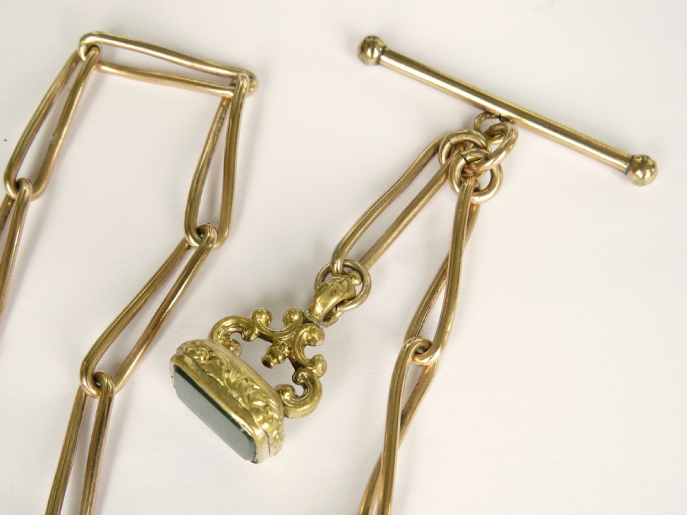 An antique Victorian rolled rose gold watch chain with elongated links, a T-bar attachment, a swivel clasp, and an ornamental fob seal with a green stone. View II