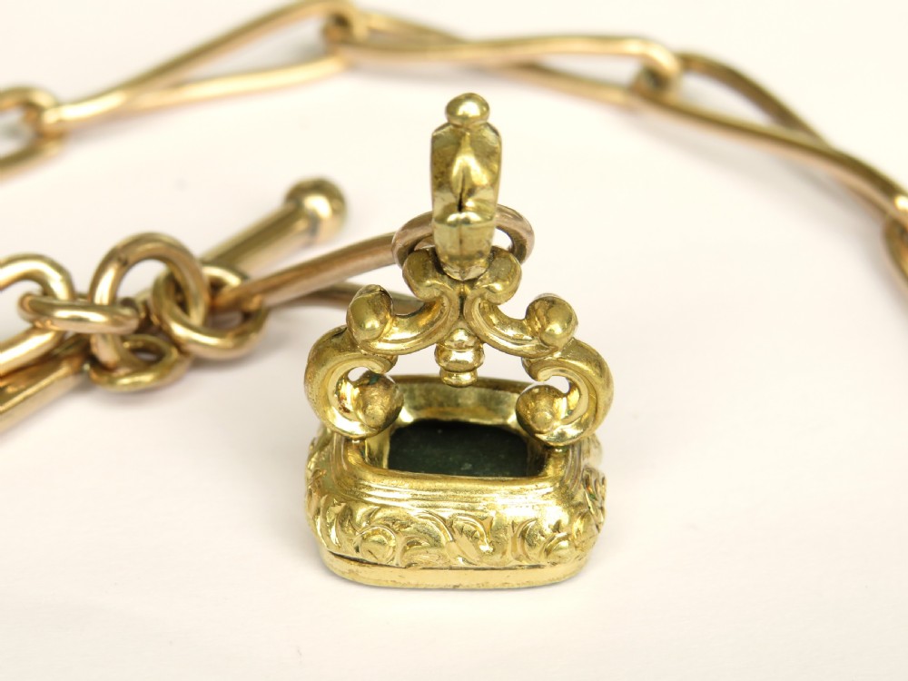 An antique Victorian rolled rose gold watch chain with elongated links, a T-bar attachment, a swivel clasp, and an ornamental fob seal with a green stone. View IV