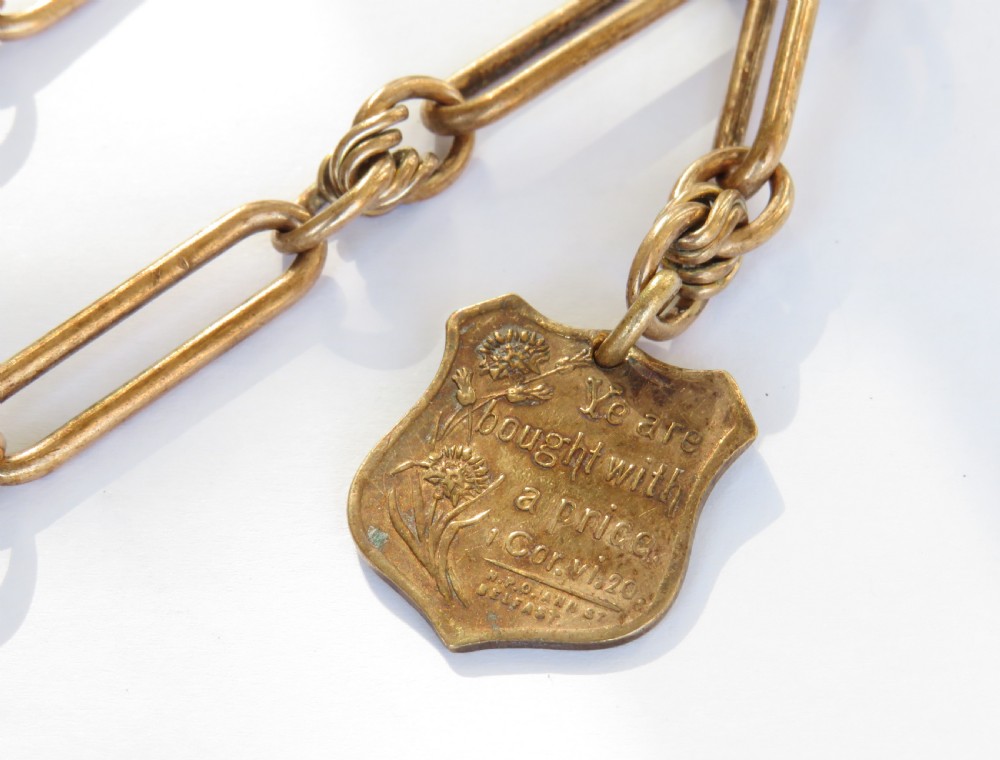 An antique rolled rose gold pocket watch chain featuring elongated open links, a T-bar, swivel clasp, and an engraved shield-shaped fob. View II