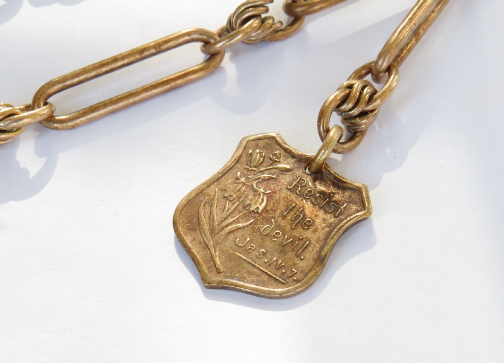 An antique rolled rose gold pocket watch chain featuring elongated open links, a T-bar, swivel clasp, and an engraved shield-shaped fob. View III