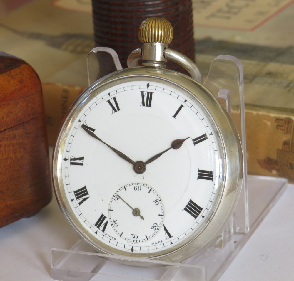 An open-face antique silver pocket watch with a white enamel dial, black Roman numerals, sub-seconds dial, and a ribbed crown.