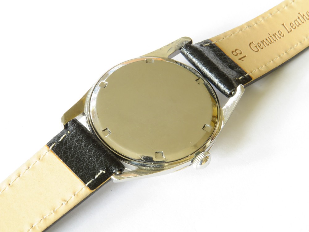 A vintage 1960s Girard-Perregaux wristwatch featuring a champagne dial, silver-tone stainless steel case, baton hour markers, and a black leather strap. View V