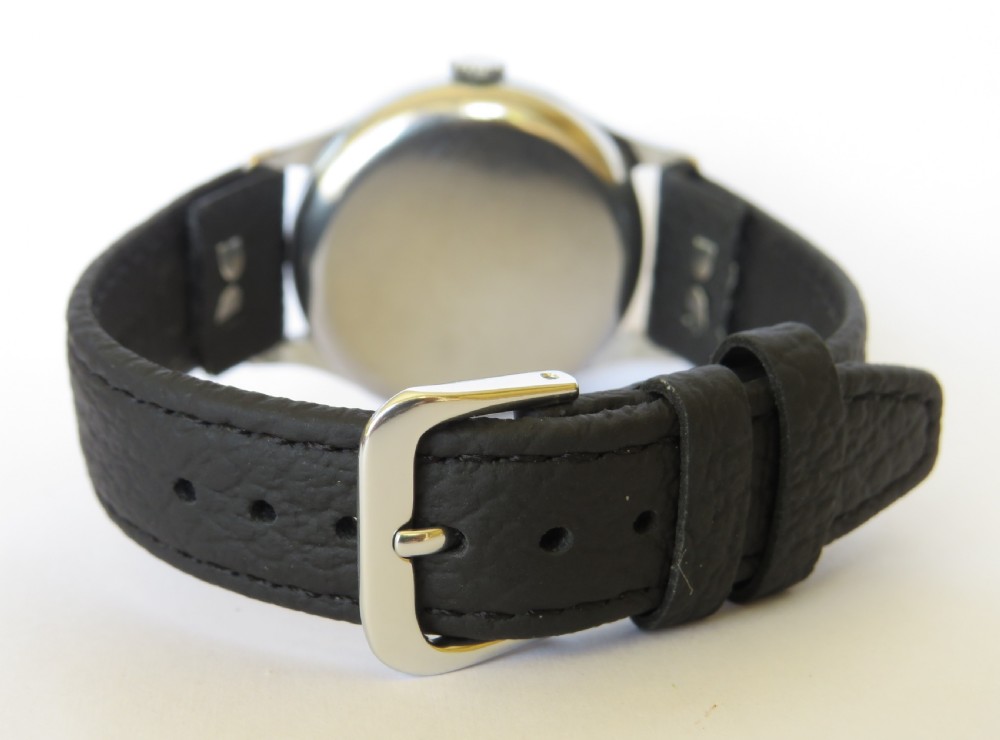 A 1950s gents Smiths Deluxe mechanical wristwatch featuring a cream dial with gold-tone Arabic numerals and a textured black leather strap. View V