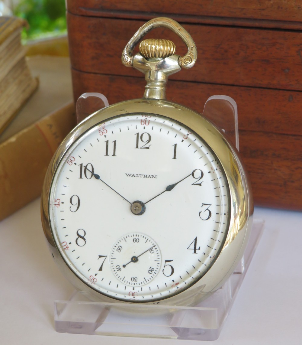 An open-face Edwardian pocket watch featuring a white enamel dial with black Arabic numerals, a subsidiary seconds dial, and a silver-toned metal case.