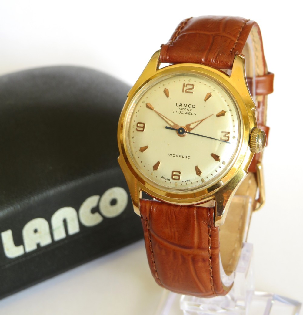 A 1950s gents Lanco Sport Swiss mechanical wristwatch featuring a gold-plated case, cream dial with arrow indices, and a textured brown leather strap.