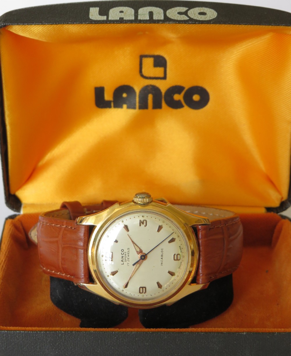 A 1950s gents Lanco Sport Swiss mechanical wristwatch featuring a gold-plated case, cream dial with arrow indices, and a textured brown leather strap. View II