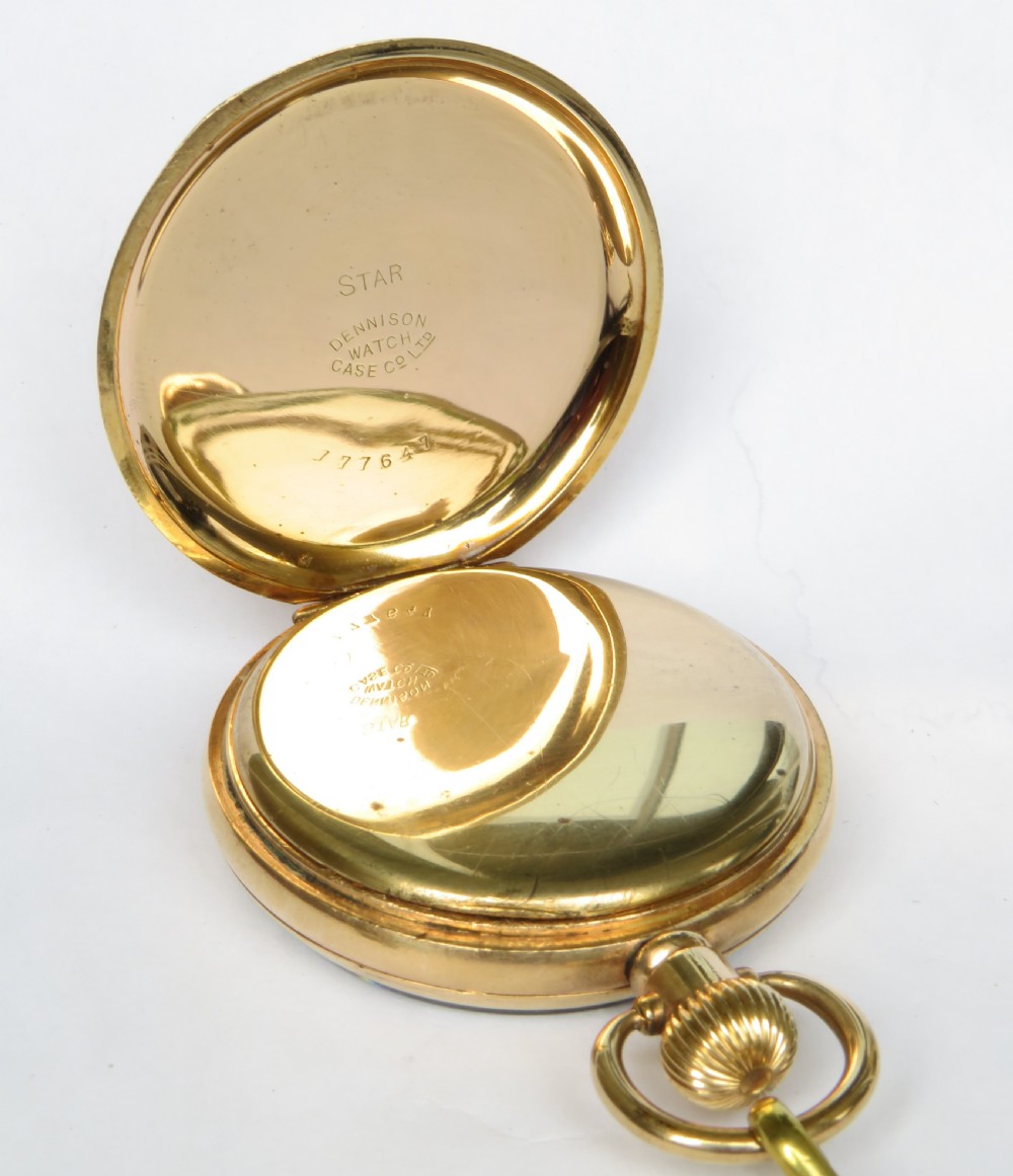 An open-face gold pocket watch featuring a white dial with Roman numerals and an accompanying black braided strap with a brass T-bar. View II