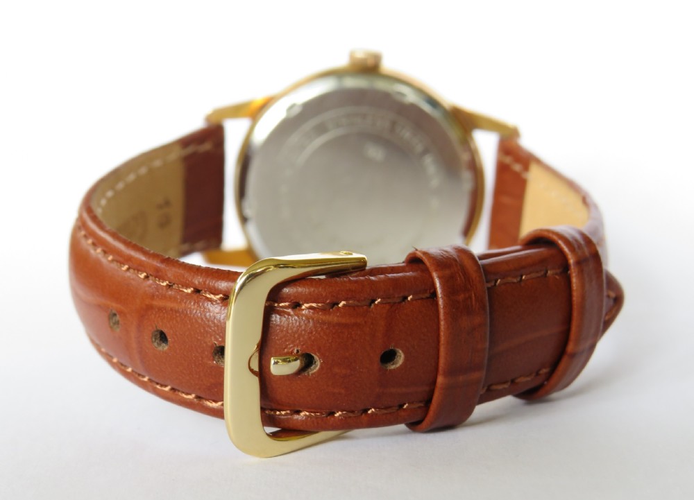 A 1960s gents Ensign gold-tone wristwatch featuring a cream dial with gold Arabic numerals and a brown leather strap. View V